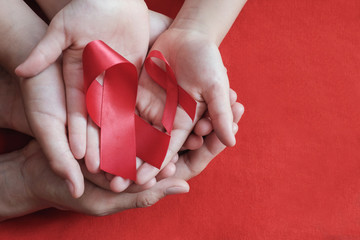Adult and children hands holding red ribbon on red background, hiv awareness concept, world AIDS...