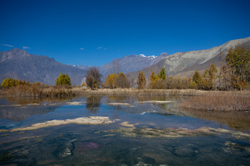 Fototapeta na wymiar Autumn trees near lake with mountains and blue sky background