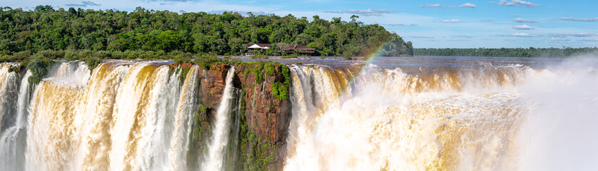 Panorama of Devil`s Throat and Salto union with blue sky, white clouds and small rainbow, Iguazu Falls, Argentina