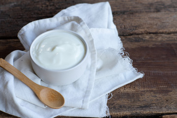 Fototapeta na wymiar Natural homemade plain organic yogurt in ceramic bowl and wood spoon on wood texture background
