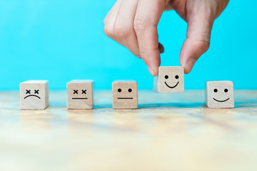 Businessman chooses a happy emoticon icons face on wooden block.