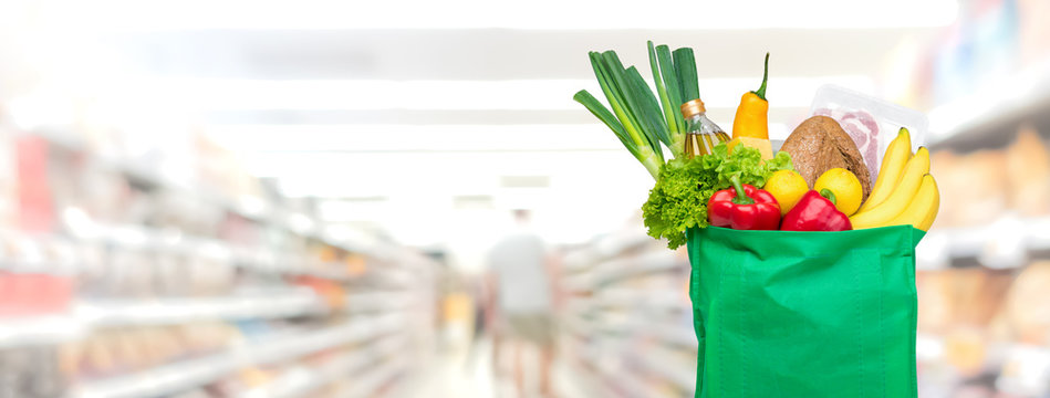 Groceries in reusable green shopping bag on supermarket banner background