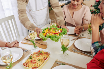 Cropped image of man bringing dishes to Christmas family dinner table