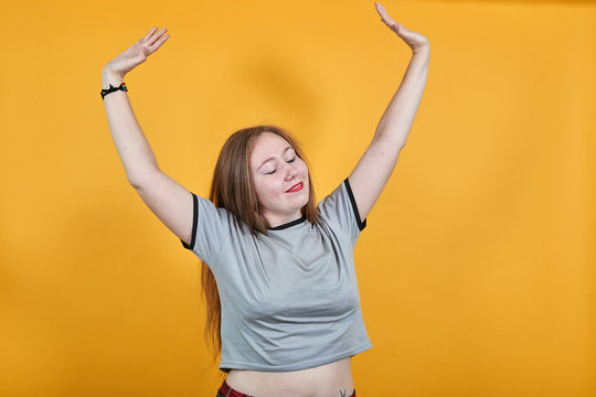 Portrait of happy joyful young woman in casual clothes rising hands with closed eyes, isolated on orange background. People sincere emotions, lifestyle concept
