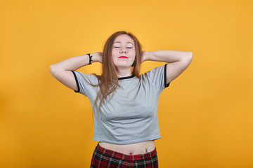 Relaxed young woman in casual clothes keeping eyes closed, with hands behind head isolated on orange wall background in studio. People sincere emotions, lifestyle concept.