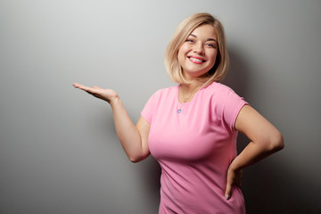 Copy space for avertisement. Portrait of happy smiling young woman pointing away against grey wall.