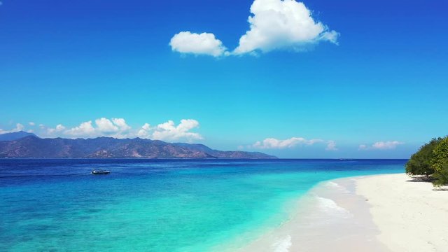 Beautiful white clouds on bright blue sky hanging over mountains surrounding azure sea with calm water, washing exotic beach in Antigua