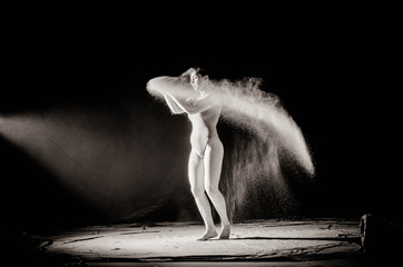 Naklejka na ściany i meble The girl with the flour on the body stretches the arms up with thrown flour on black background black and white image