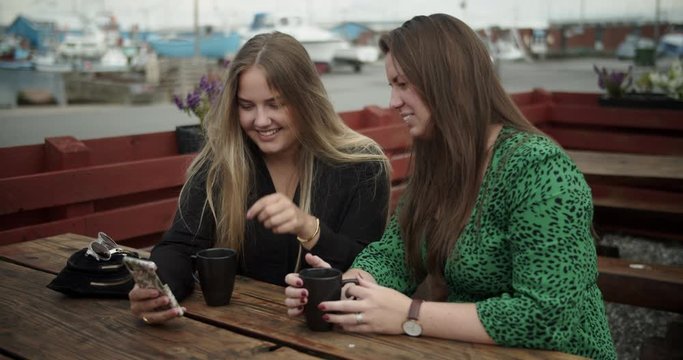 Girlfriends having a good time drinking coffee and looking on smartphone. Cinematic lifestyle scene perfect for travel or corporate video projects.