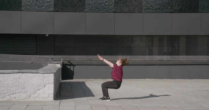 Young female gymnast doing a backflip, girl doing a somersault and series of flips, 4k slow motion, cityscape, side view.