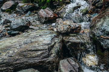 Clear spring water flows on beautiful stony pile slope. Boulder stream with small mountain creek. Wet shiny stones close-up. Nature background with small highland brook. Clear water stream on boulders