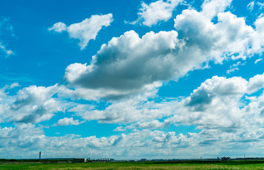 Fototapeta na wymiar Landscape green grass field and wire fence of the airport and beautiful blue sky and white fluffy clouds. Nice weather. Nature landscape. Area around the airport. Fence for safety. Airport building.