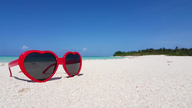 Color Red- Heart Shape Sunglasses at the Seashore With Clear Sky And Green Trees At the Background in Seychelles - Close Up Shot
