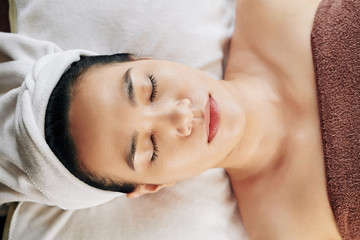 Fototapeta na wymiar Young beautiful Vietnamese woman resting with eyes closed after refreshing skin treatment, view from above