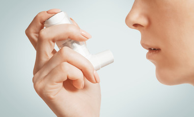 Woman holding medical asthma inhaler near her face.