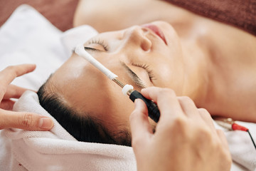 Beautician touching forehead with equipment for micronutrient treatment