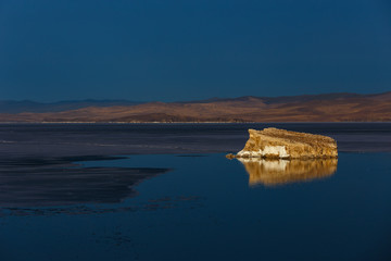 Small rocky island at Baikal lake with its reflection with melting ice