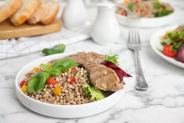 Tasty buckwheat porridge with meat on white marble table