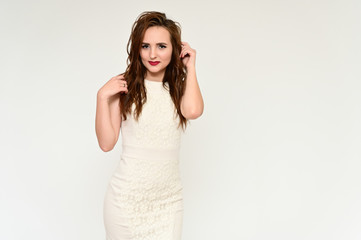 Fototapeta premium A concept of a nice young pretty brunette girl with a beautiful hairstyle and great make-up talking to the camera. Photo Portrait of a girl on a gray background in a beige dress in various poses.