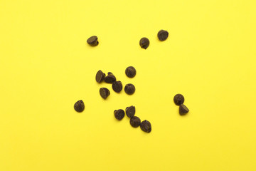 Delicious chocolate chips on yellow background, top view