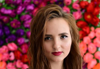 Obraz na płótnie Canvas The concept of beauty, fashion, makeup, cosmetics. Portrait of a pleasant young pretty brunette girl with a beautiful hairstyle, great makeup, long curly hair against a background of flowers.
