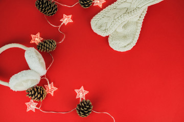 Festive Christmas and New Year background with garland in form of stars, cones, warm headphones, knitted mittens, confetti on red background. Top View. Flat lay. Concept of preparation for holidays.