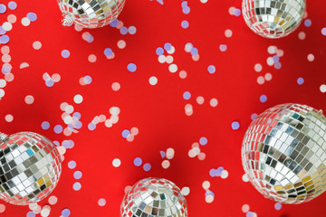 Disco mirror ball Christmas tree toy on a bright festive red background with scattered confetti. Christmas and New Year holiday concept. View from above. Flat lay.