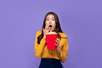 Excited Asian woman holding popcorn and gasping while watching movie