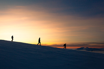 Fototapeta na wymiar Three men descend from the mountain at sunset in winter