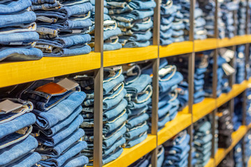 Neat stacks of folded jeans on the shop shelves in the showroom or store. Clothes storage. Shopping...