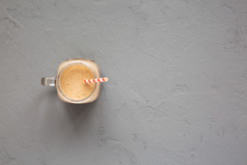 Homemade smoothie with coffee, oat and banana in a glass jar mug on a gray background, top view. Overhead, from above, flat lay. Copy space.
