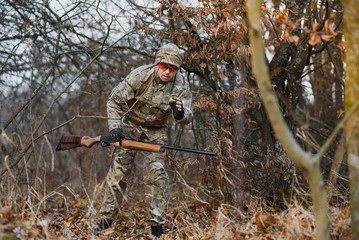 hunting, war, army and people concept - young soldier, ranger or hunter with gun walking in forest