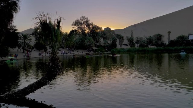 Sunset at Huacachina Oasis. Relaxing scene of water in a natural oasis. Sun behind the mountain dune. Ica region, Peru  