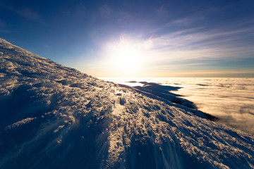 View from the slope of the mountain at sunset, snow texture, clouds below the mountain
