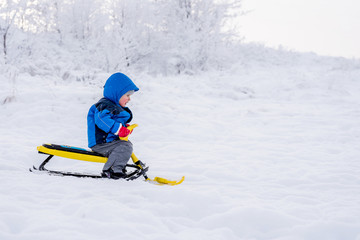 little child riding a snow scooter in winter
