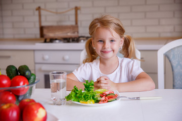 blonde baby girl eating vegetables in the kitchen