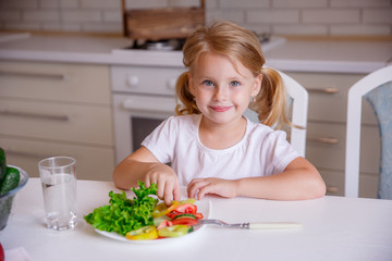 Obraz na płótnie Canvas blonde baby girl eating vegetables in the kitchen