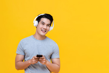 Smiling young handsome Asian man listening to music online from smartphone