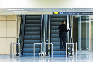 The alone woman on the escalator or moving staircase with inscription departure in English and Chinese in the international airport or railway station from the back moving upstairs with luggage