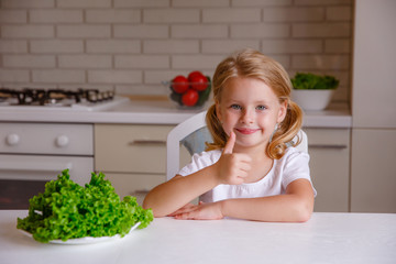 blonde baby girl eating vegetables in the kitchen