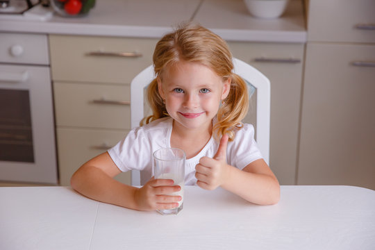 a little girl sits at home at the kitchen table and drinks milk for breakfast, raises her finger up, super, recommends