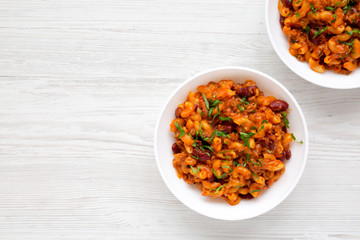 Homemade Chili Mac and Cheese with Parsley in white bowls over white wooden background, overhead view. Flat lay, top view, from above. Copy space.