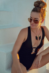 Beautiful fashionable woman wearing sunglasses and wings jewelry set, posing outdoor on white wall background - Image