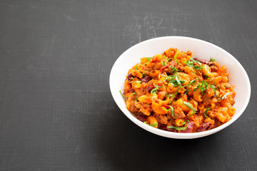 Homemade Chili Mac and Cheese with Parsley in a white bowl over black surface, low angle view. Space for text.