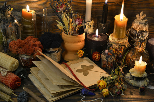 Still life with open book, four-leaf clover, candles and dry flowers on witch table.