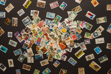 Various old postage stamps scattered on a dark background - obrazy, fototapety, plakaty
