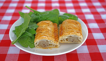 Selective focus of a sausage roll, cut in two, with green salad leaves on a white plate on a red checked background
