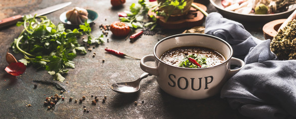 Bowl with lentil soup on rustic kitchen table background with spoon and various ingredients. Wide...