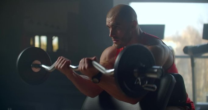 male athlete lifts a barbell with weight sitting on a bench. Slow motion exercise of the hands