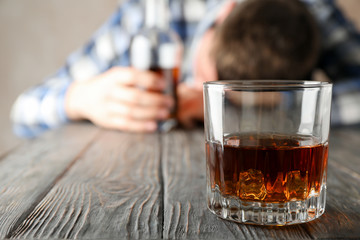 Drunk man holds bottle on wooden table with glass of whiskey, copy space